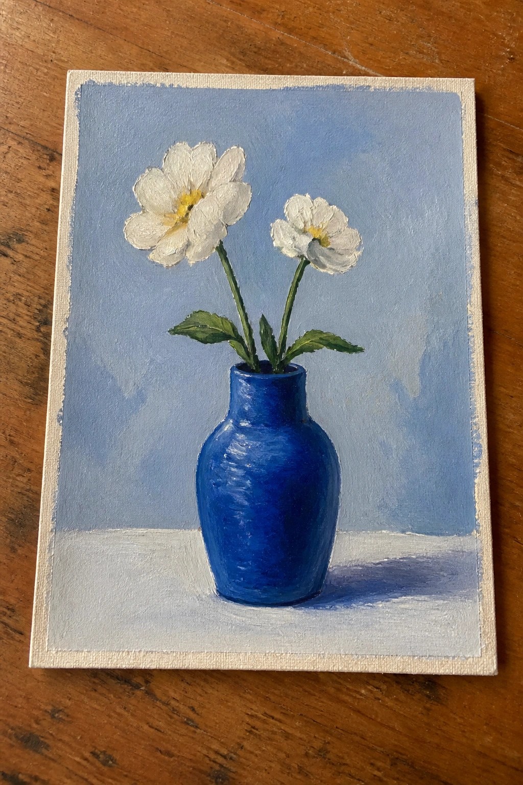 Two white flowers in a blue vase on a white surface against blue backdrop