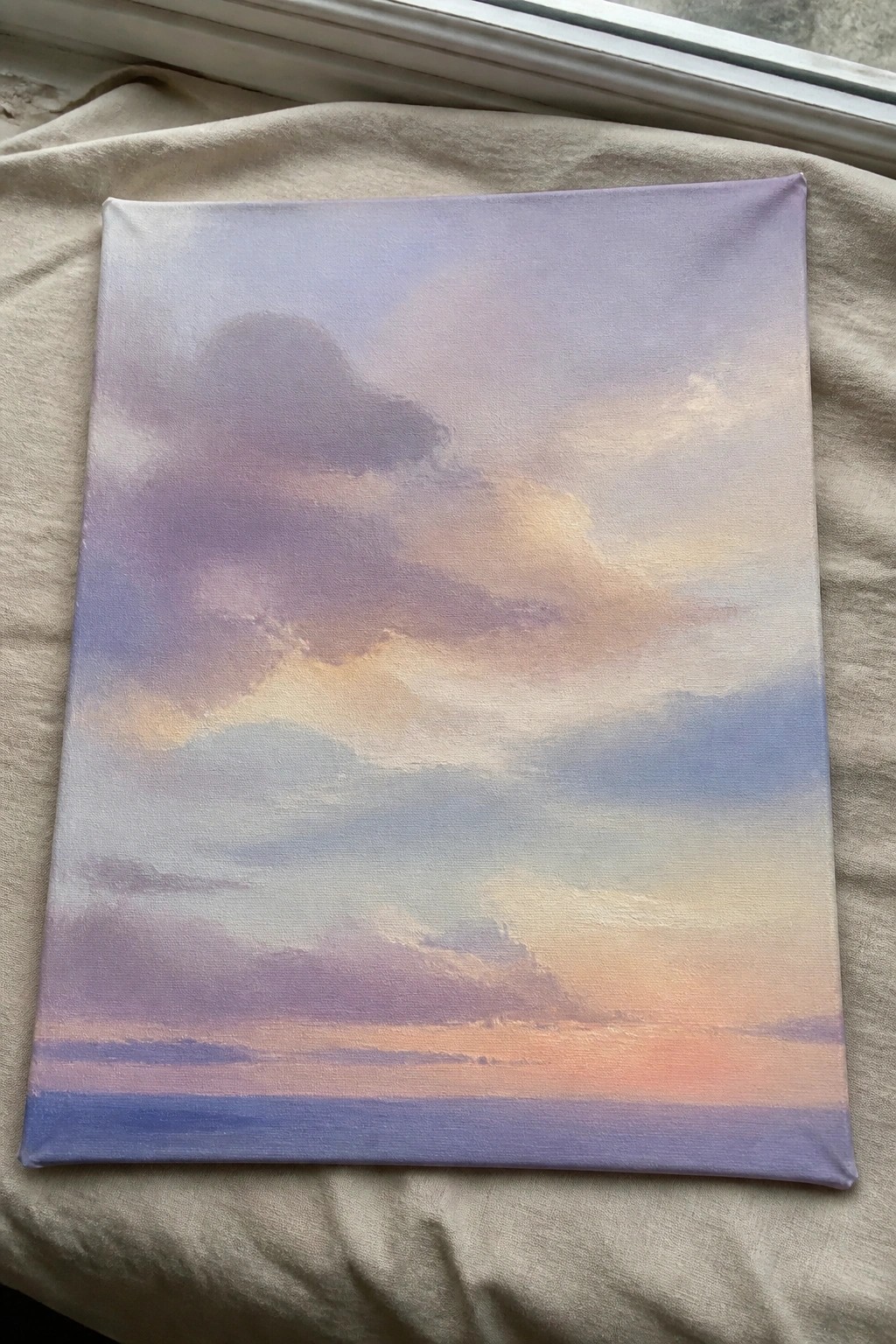 Pastel cloud painting on canvas resting on rumpled beige fabric by window