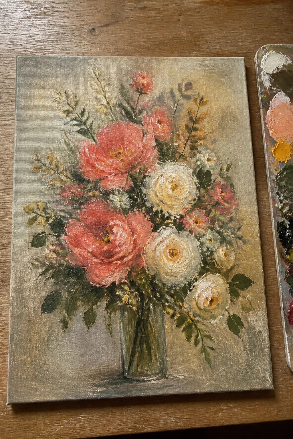 Oil painting of pink peonies and white roses in glass vase with palette nearby