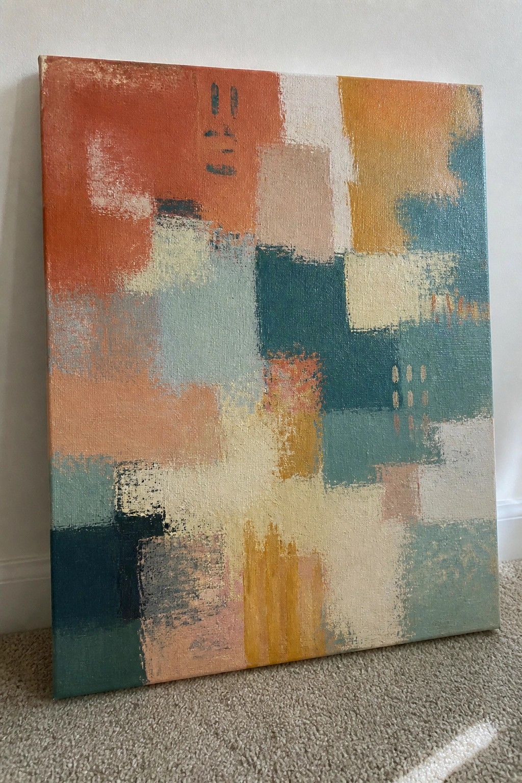 Abstract painting with orange, teal, and yellow brushstrokes leaning against wall on carpet