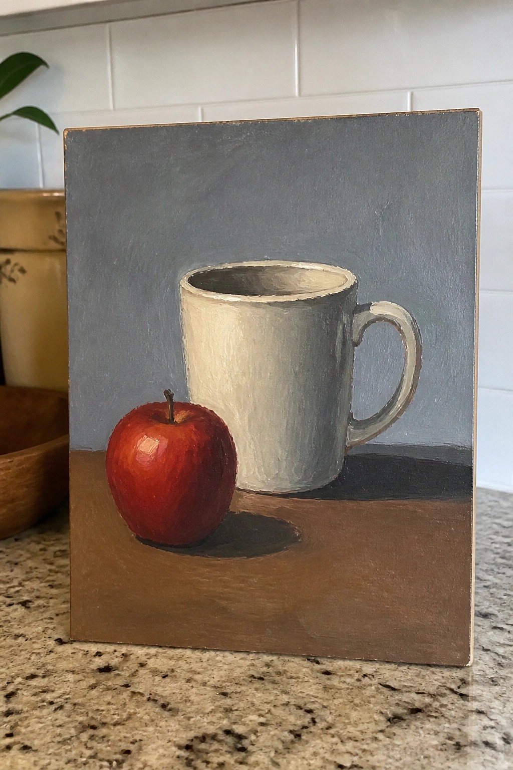 Still life painting of red apple beside white mug on brown surface with shadows