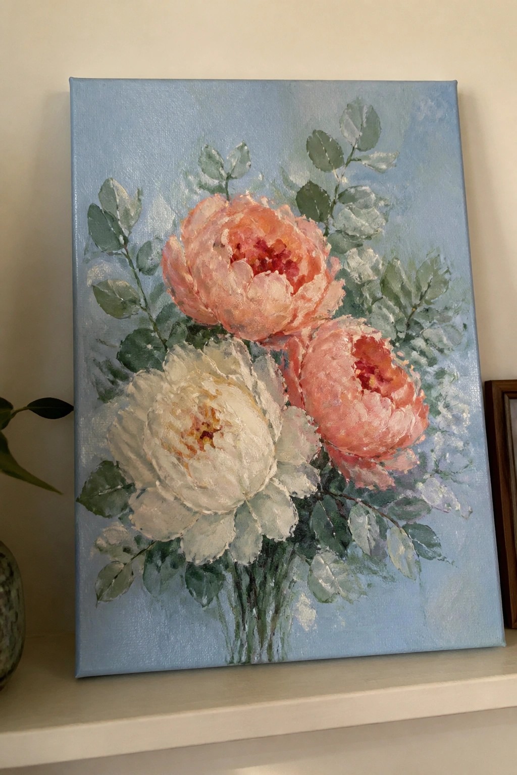 Oil painting of three white and coral peonies with green leaves on blue canvas