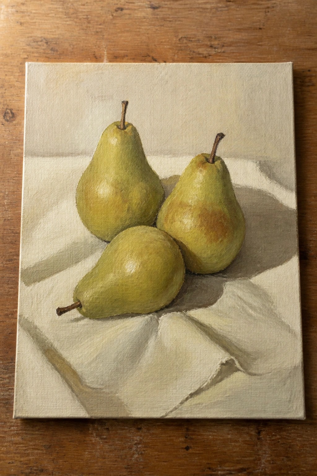 Three green pears on white draped cloth atop wooden surface in oil painting