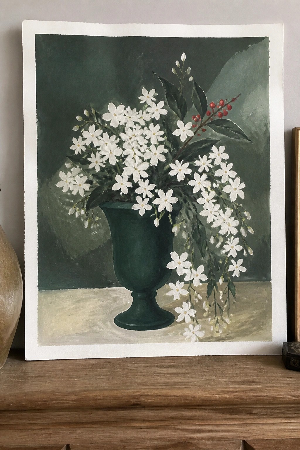 Still life of white flowers with red berries in dark green vase on wood.