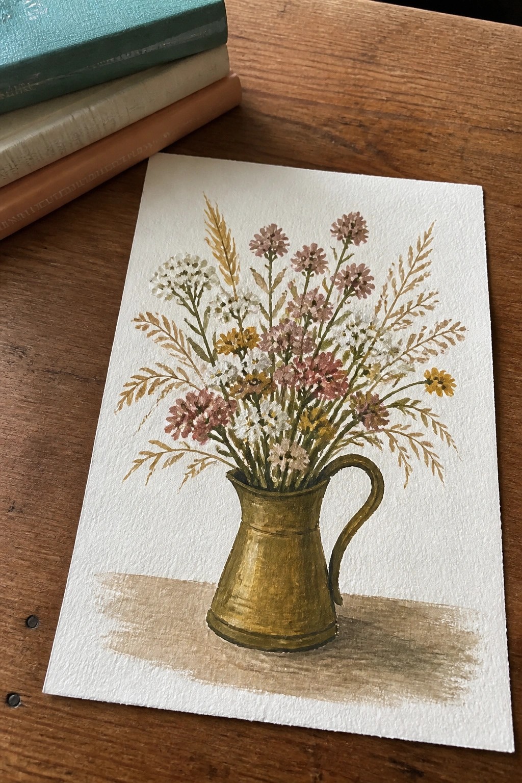 Watercolor of pink, white and yellow wildflowers in gold pitcher on wood