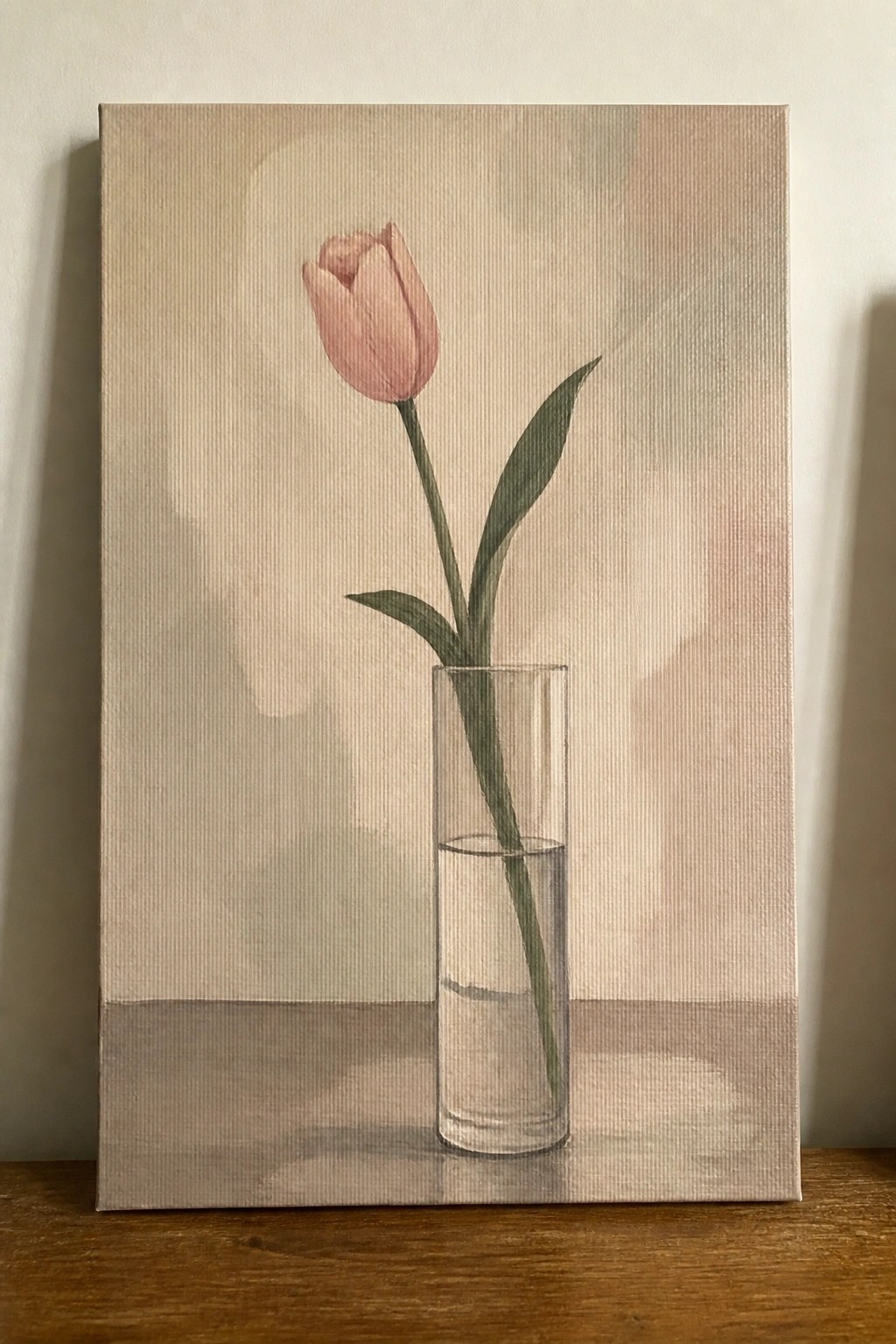 Pink tulip with green leaves in clear glass vase with water on canvas.