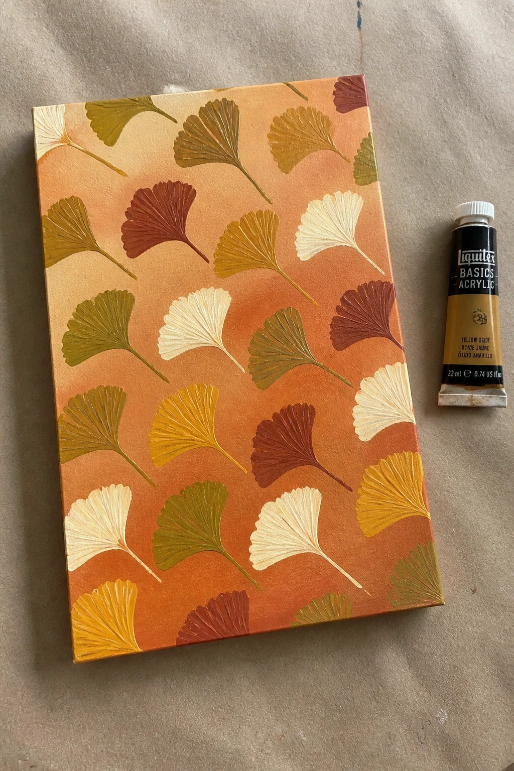 Textured canvas with colorful ginkgo leaves in autumn tones beside yellow paint tube