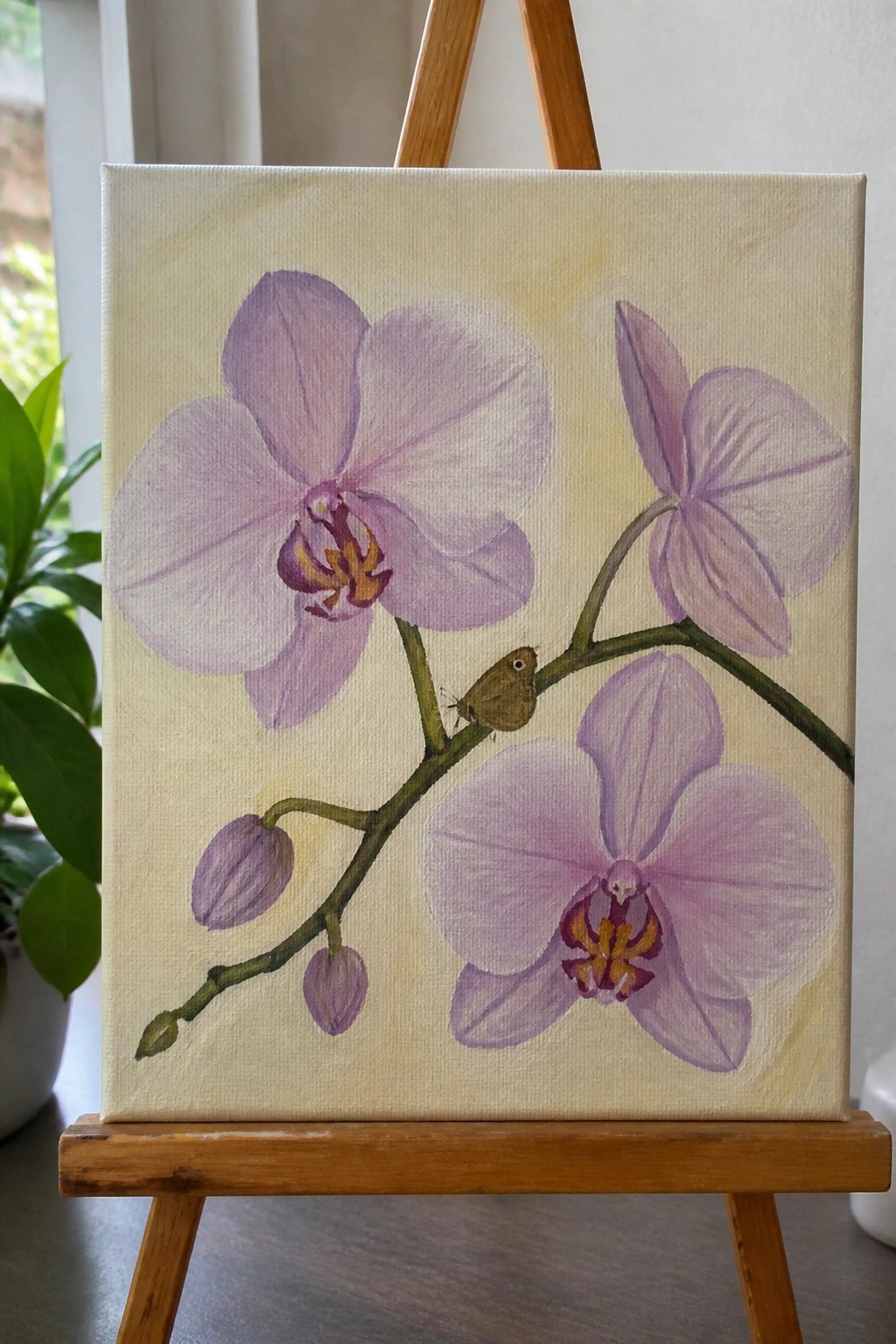 Painting of light purple orchids with buds and small moth on wooden easel.