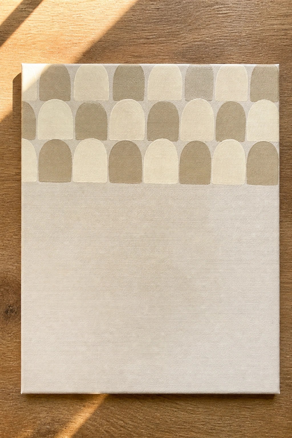 Canvas with rows of beige arches on upper half and plain white lower section on wood