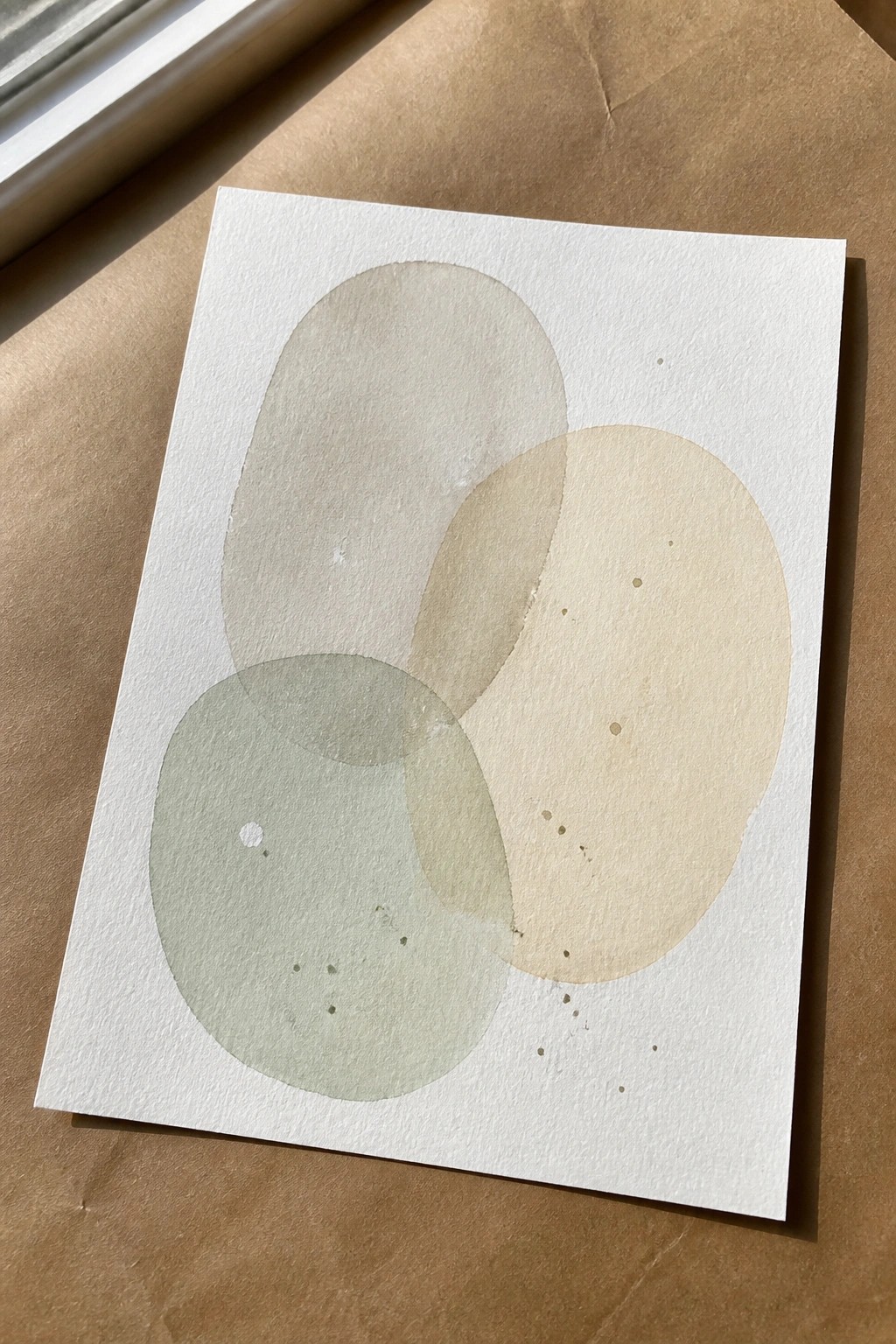 Abstract watercolor with three overlapping circles in beige, green, and yellow on white paper.
