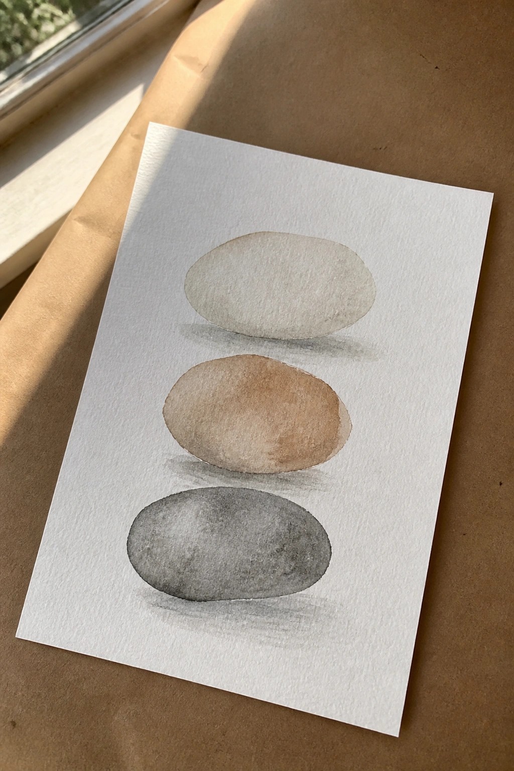 Watercolor painting of three stacked ovals in beige, brown, and gray with shadows.