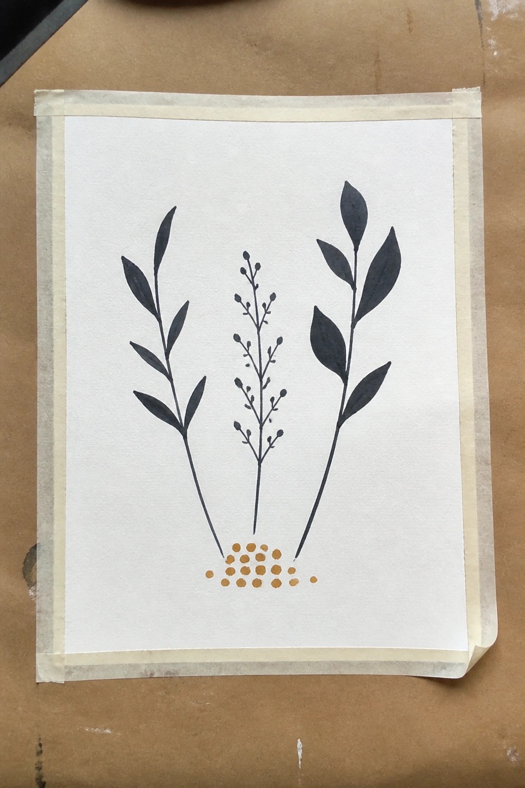 Three black plant stems with golden dots on white paper taped to brown surface