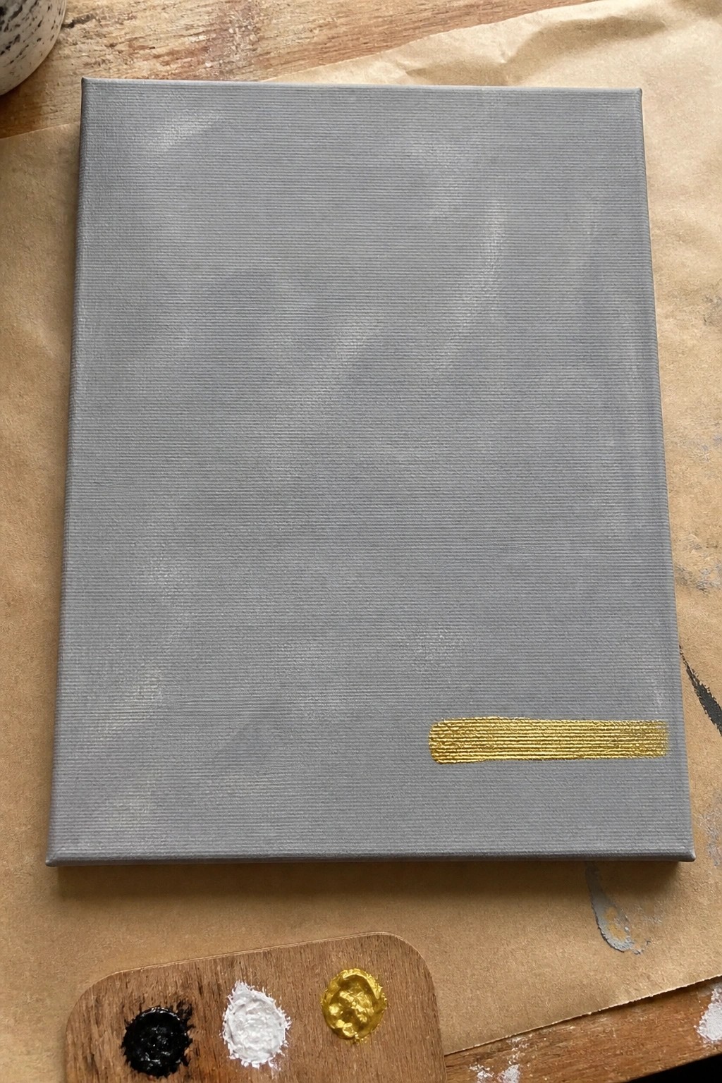 Gray canvas with gold brushstroke beside palette of black, white, and gold paint