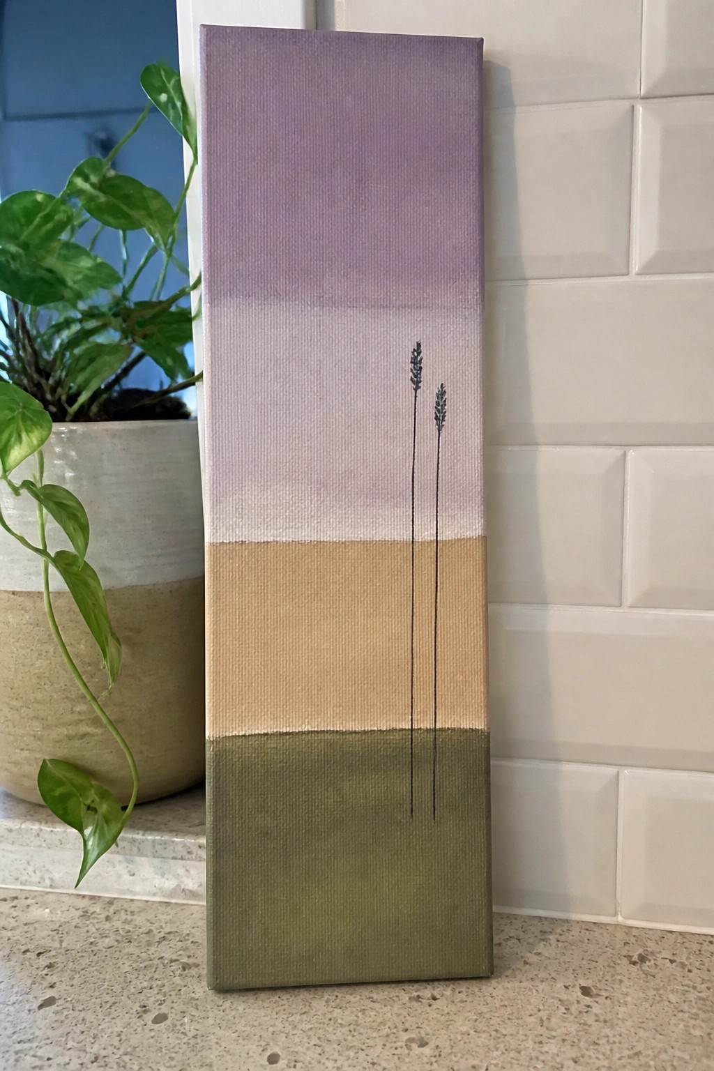 Vertical canvas with lavender sprigs on purple-to-beige-to-green gradient beside potted plant