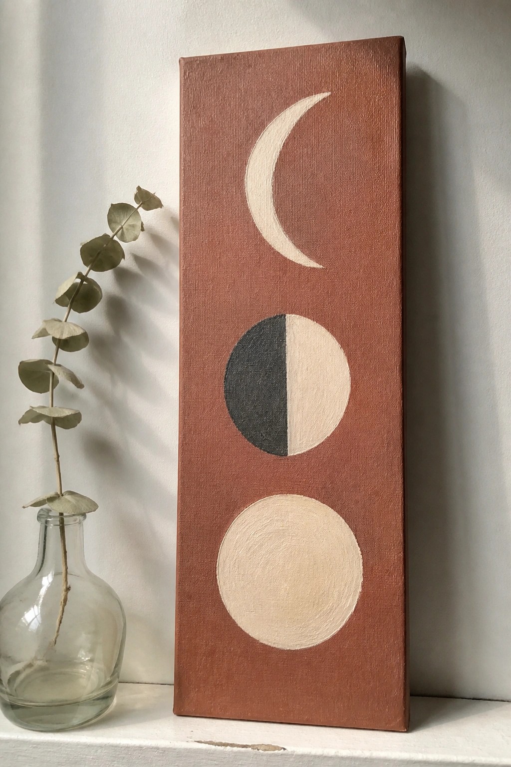 Minimalist terracotta canvas with crescent moon, split circle, full circle beside eucalyptus vase