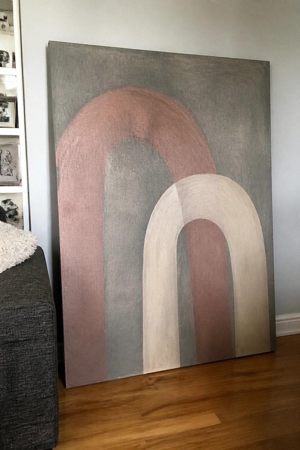 Large abstract painting with overlapping arches in muted pink, gray, and beige on wood floor.