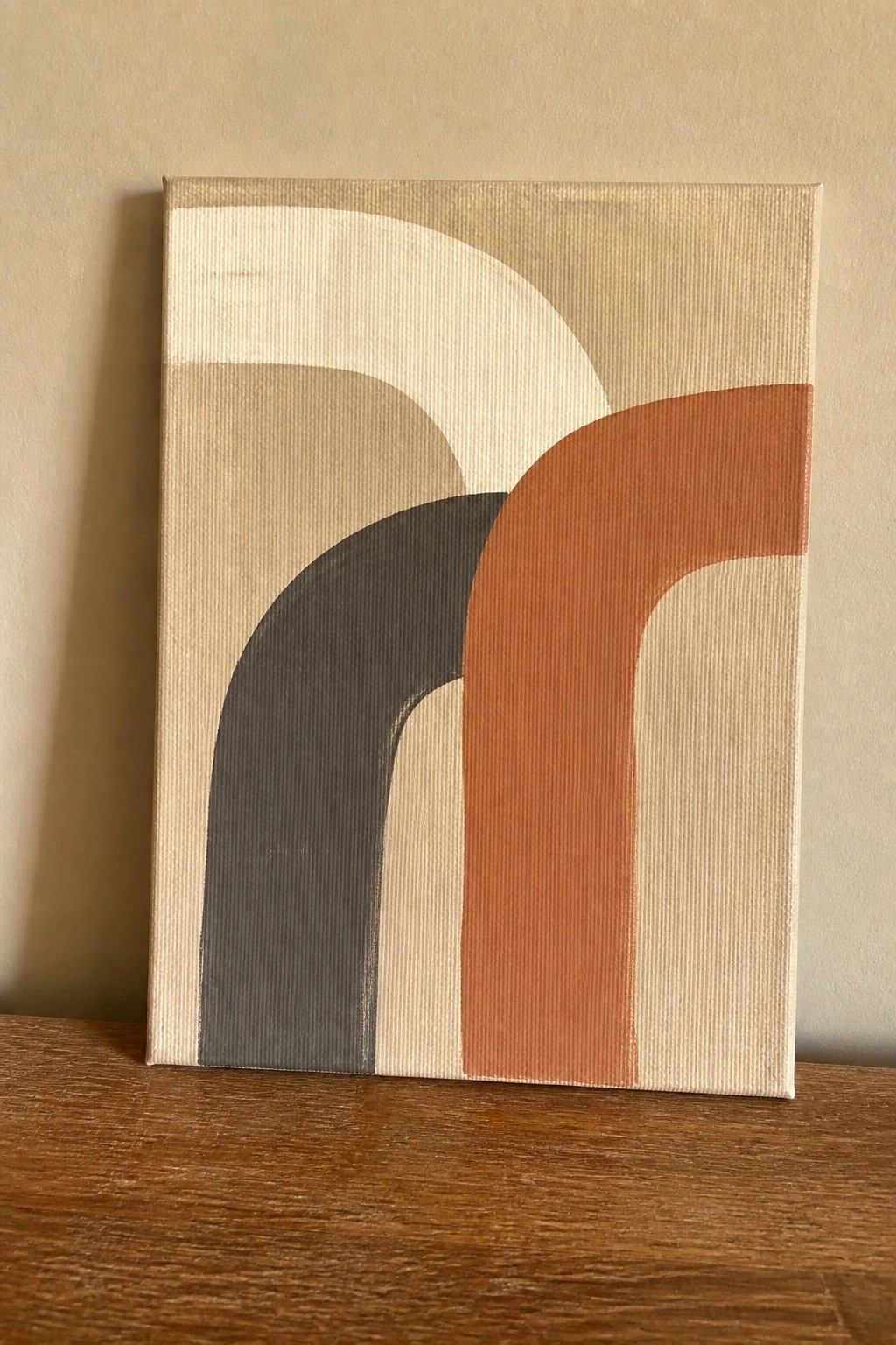 Abstract canvas with overlapping arches in beige, gray, and orange on wooden surface.