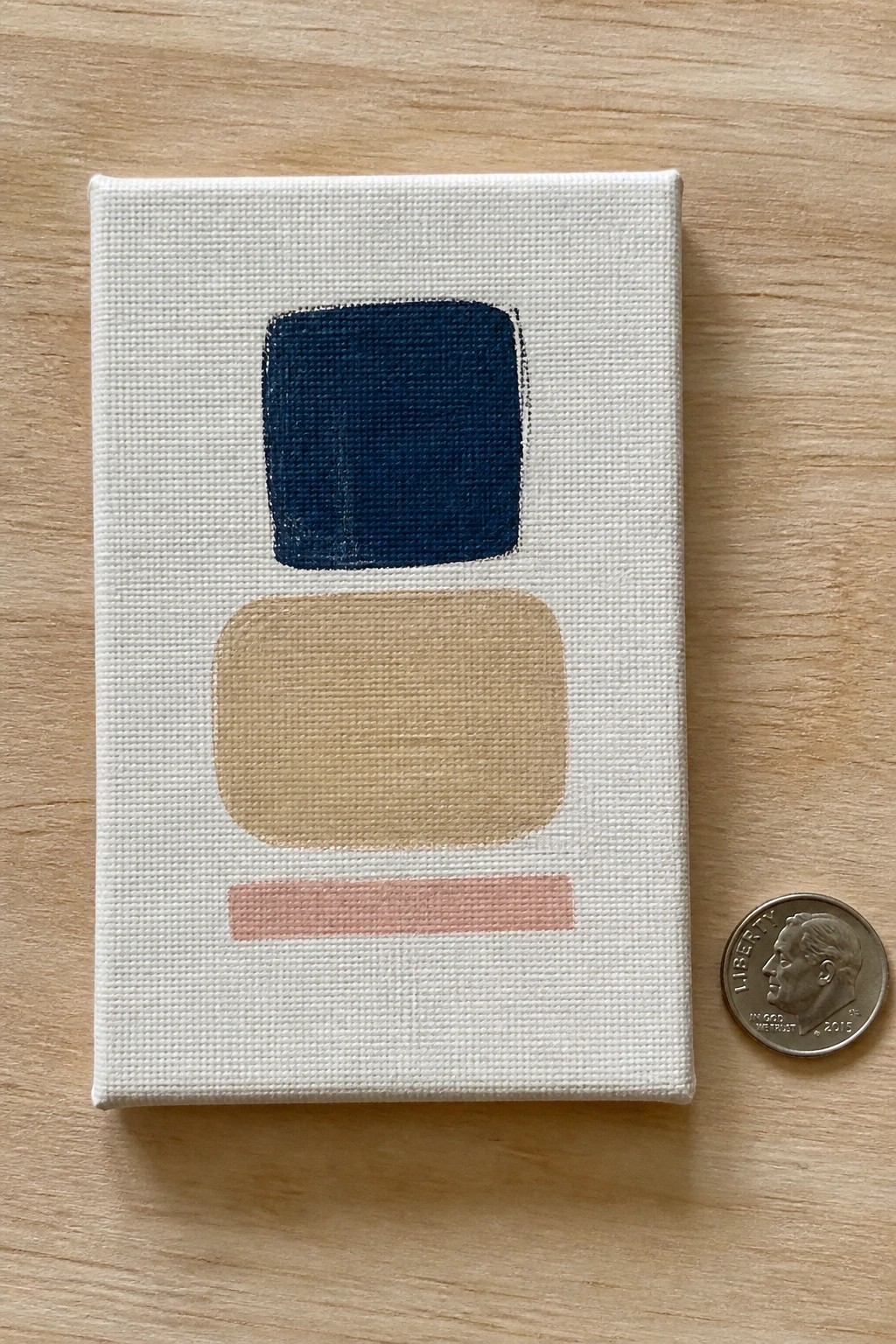 Small abstract canvas with navy square, beige shape, pink stripe beside a dime