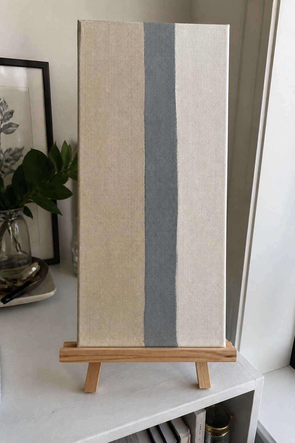 Minimalist canvas with vertical beige and gray stripes on wooden easel stand.