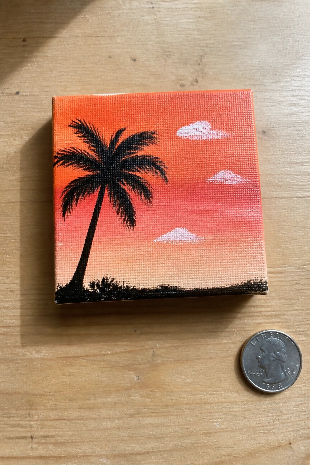 Mini canvas sunset painting with palm tree silhouette beside a quarter coin.