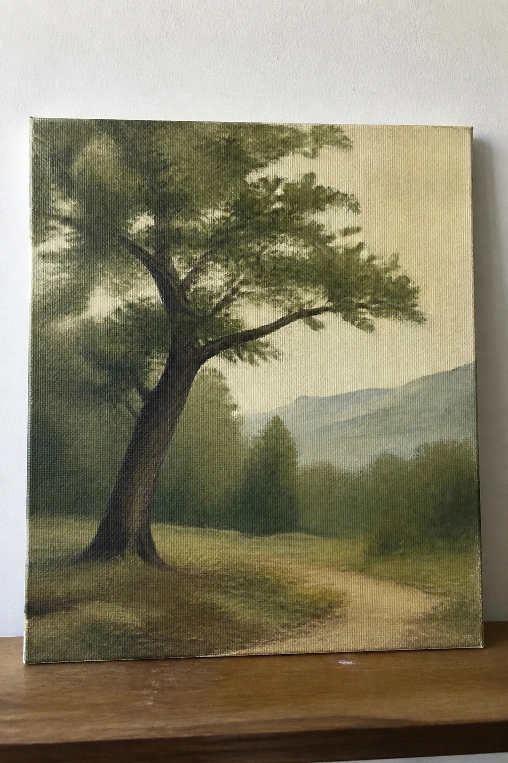 Landscape painting of large tree beside winding dirt path amid misty green hills.