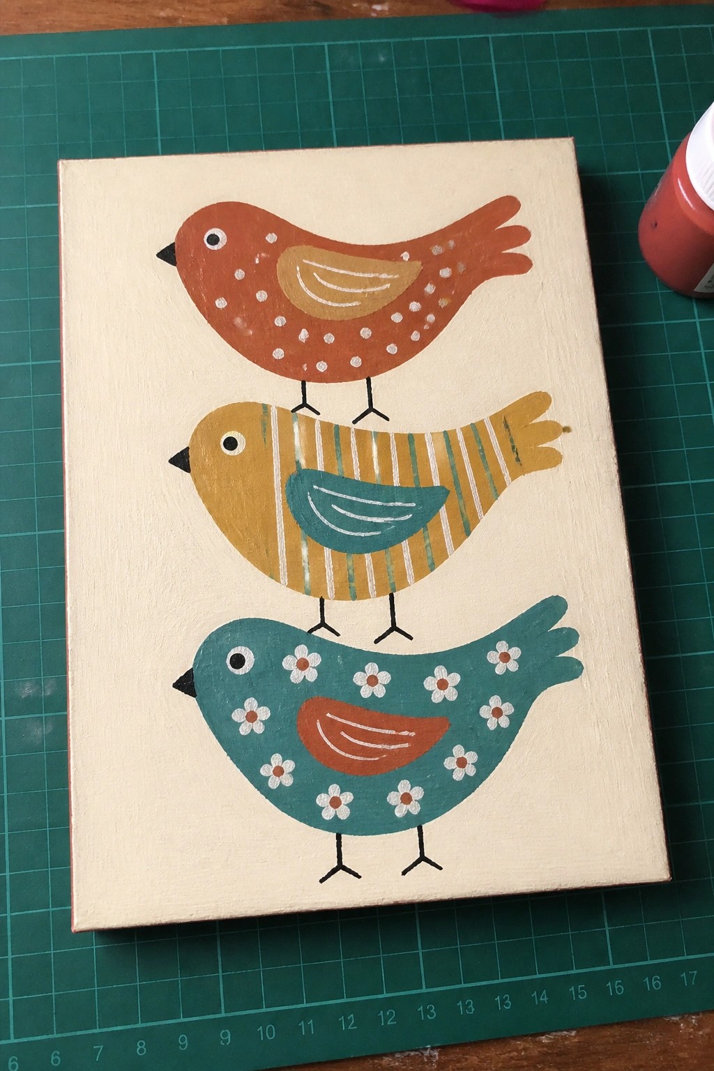 Three stacked folk-art birds in orange, yellow, and teal on canvas.