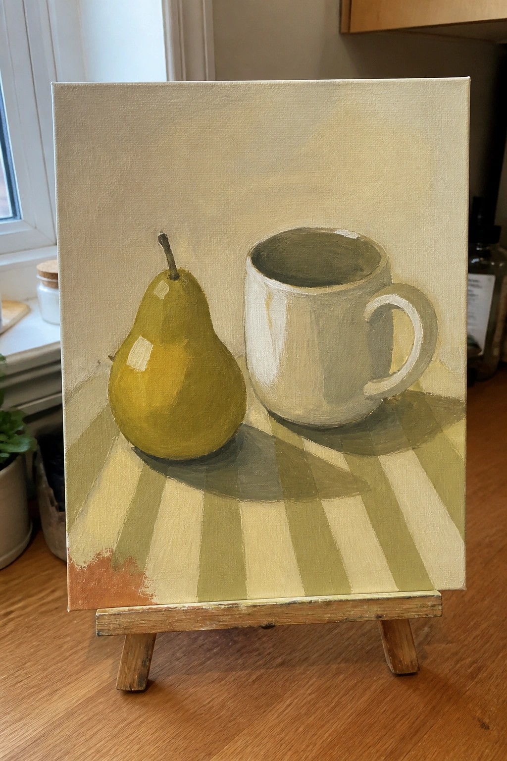 Still life painting of yellow-green pear beside white mug on striped tablecloth