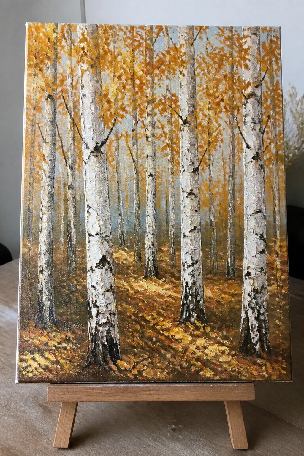 Painting of autumn birch forest with white trunks, golden leaves on wooden easel