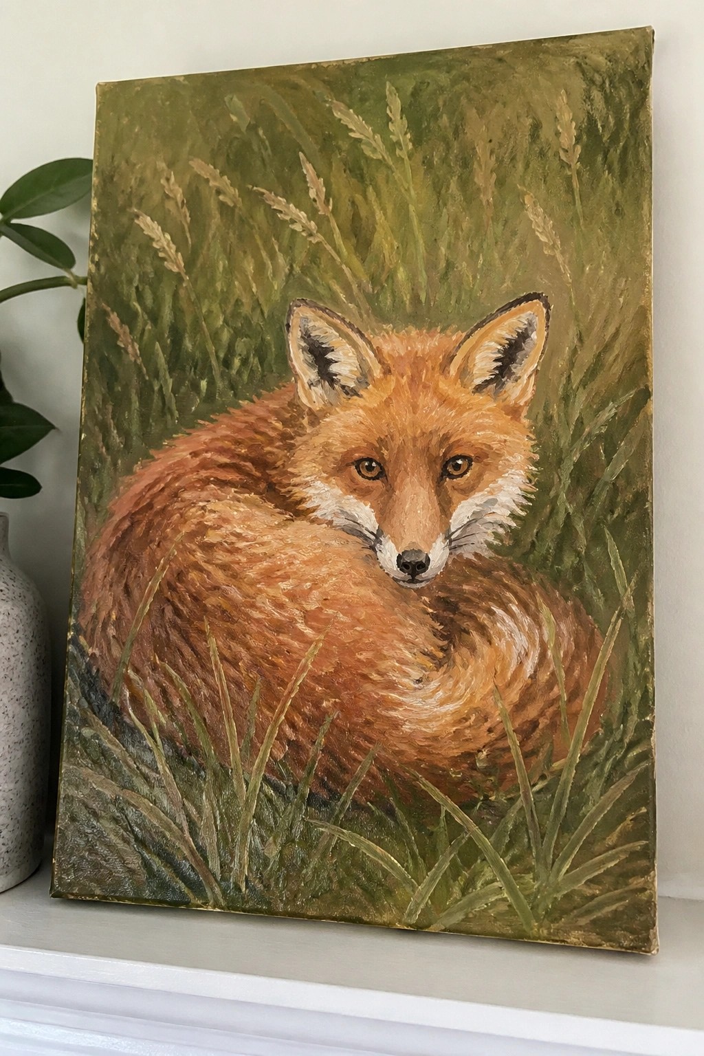 Red fox curled in grass on painting beside speckled vase on ledge