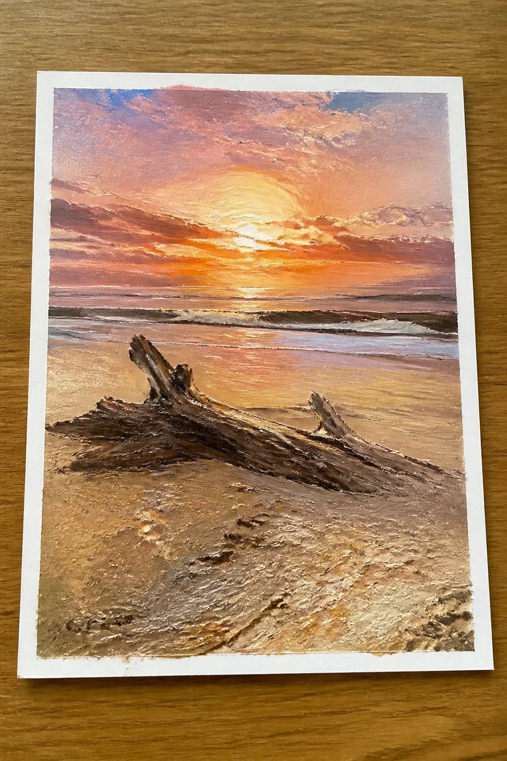 Vibrant sunset over ocean with pink-orange clouds, sun reflection, and driftwood on wet sand.