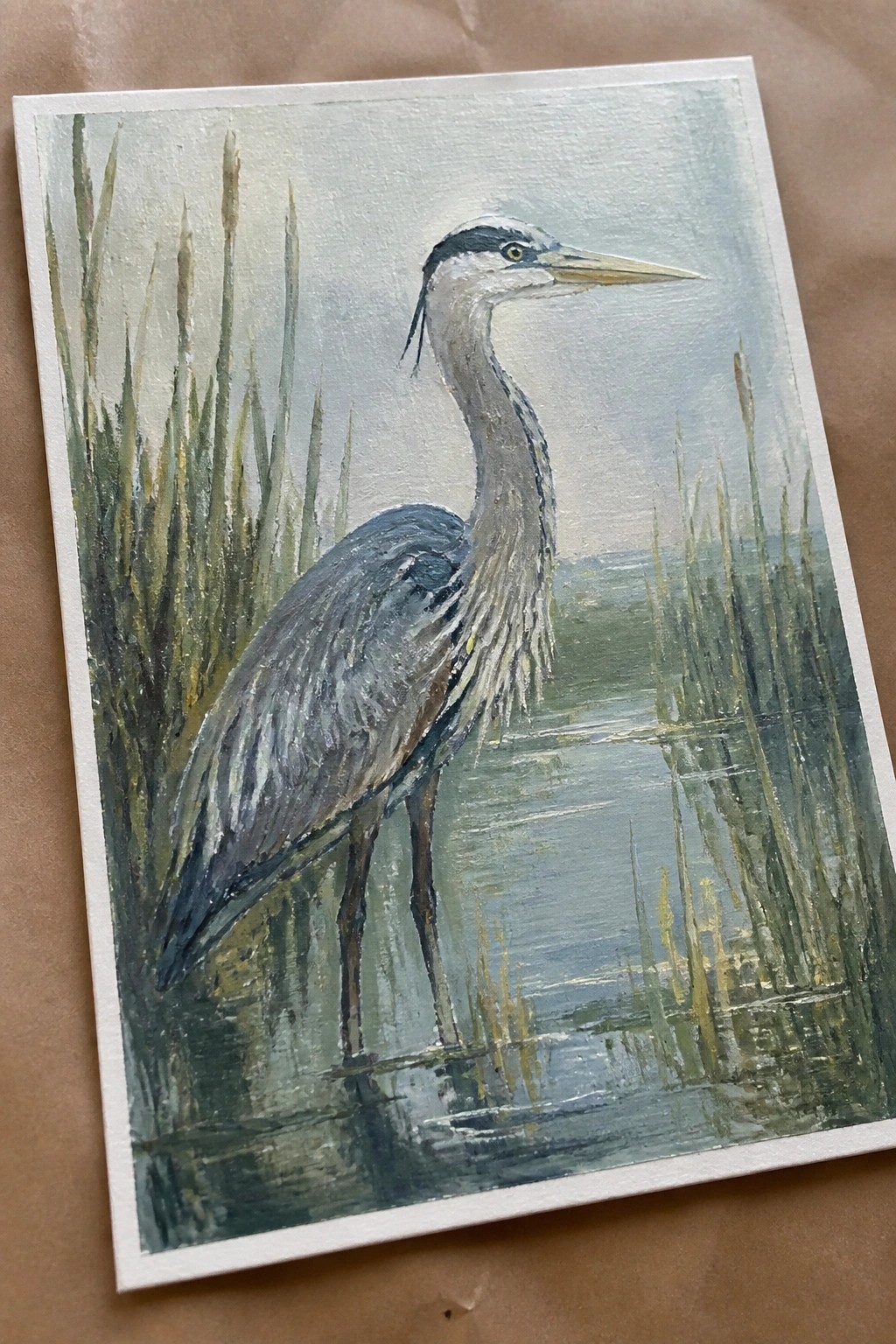Great blue heron stands in shallow water amid tall green reeds