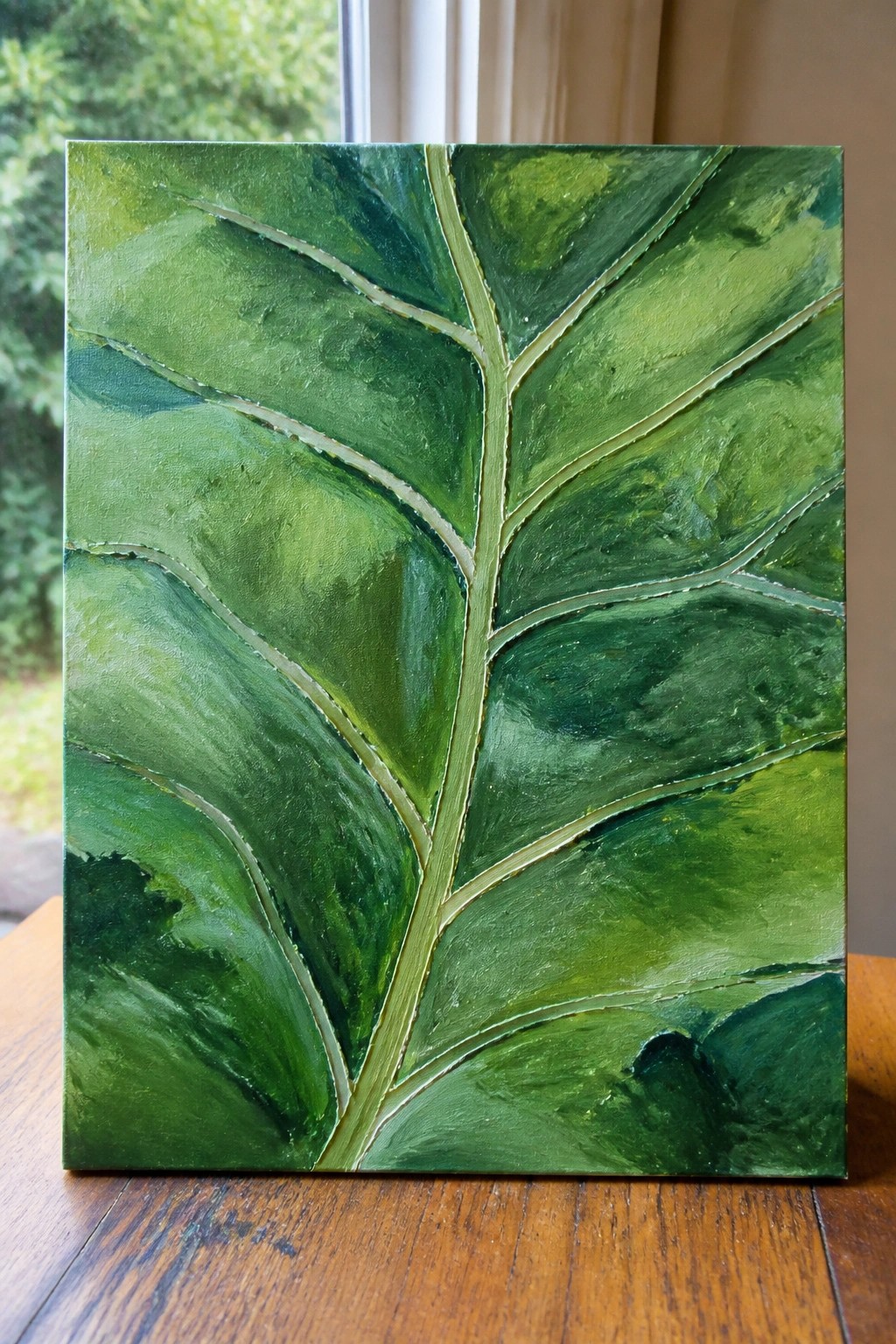 Textured green leaf painting with prominent veins on wooden table near window