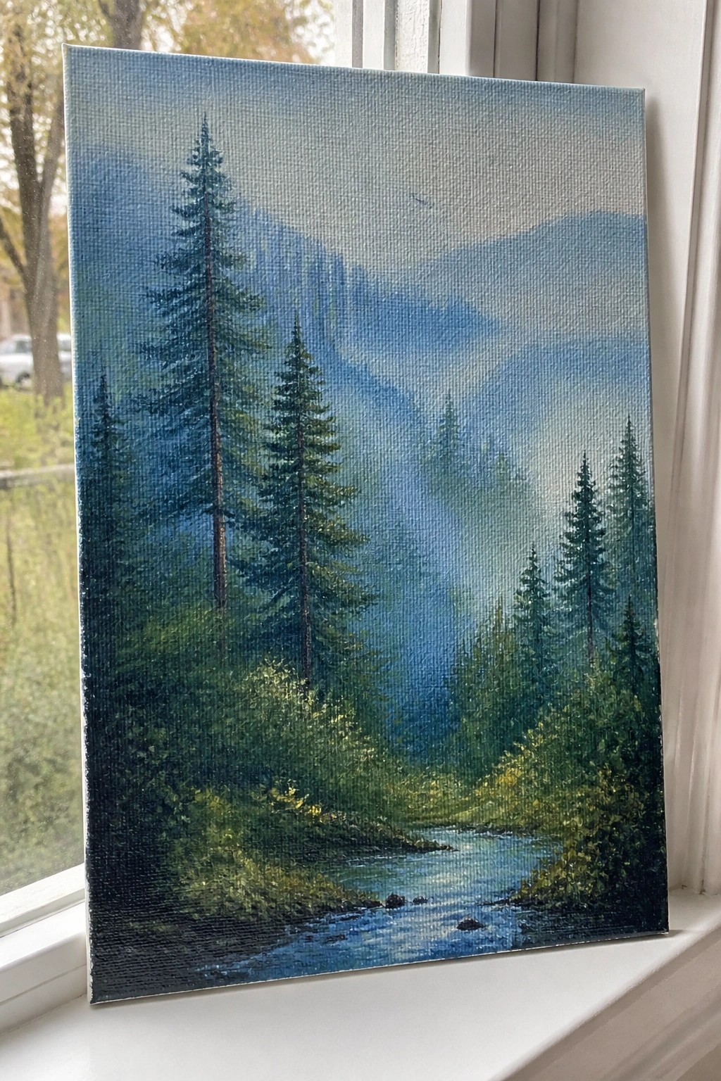 Misty blue forest landscape painting with river on white windowsill