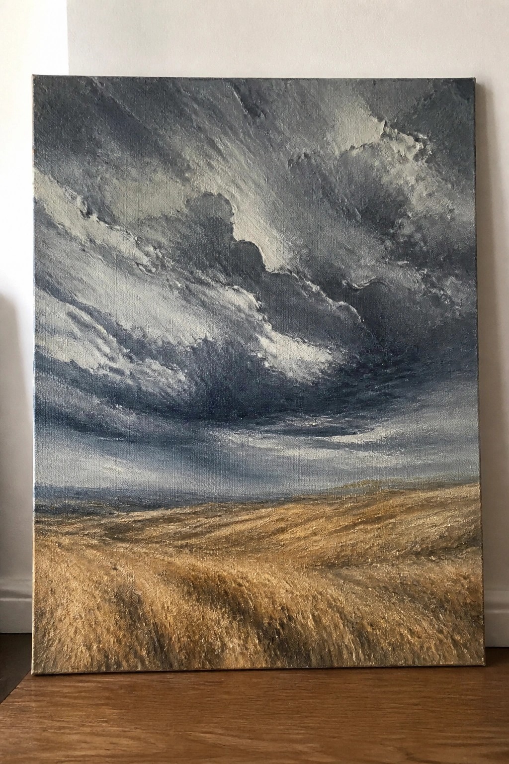 Stormy dark clouds swirl above a textured golden field in expressive landscape painting.