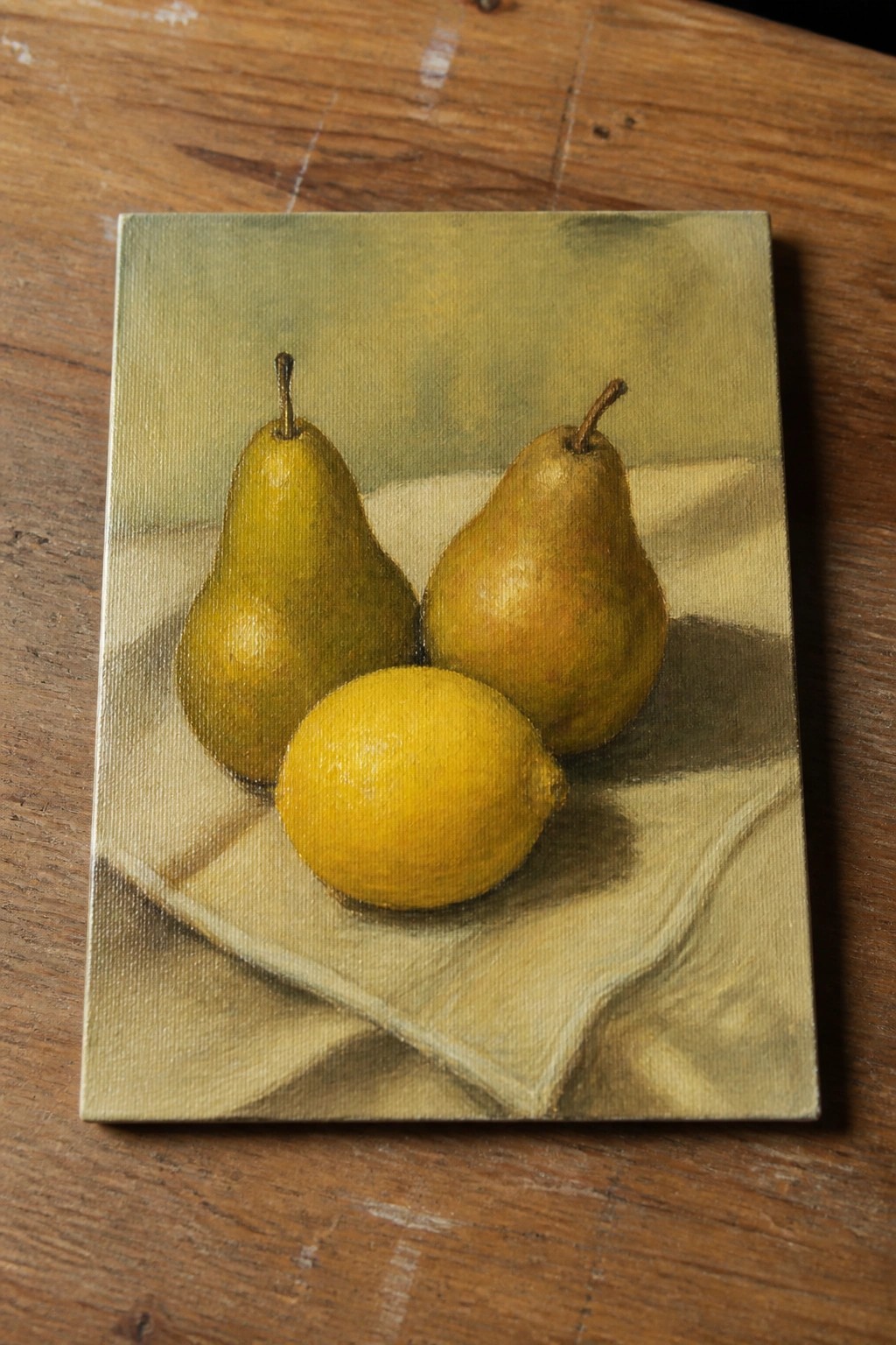 Still life painting of two pears and a lemon on draped cloth over wood