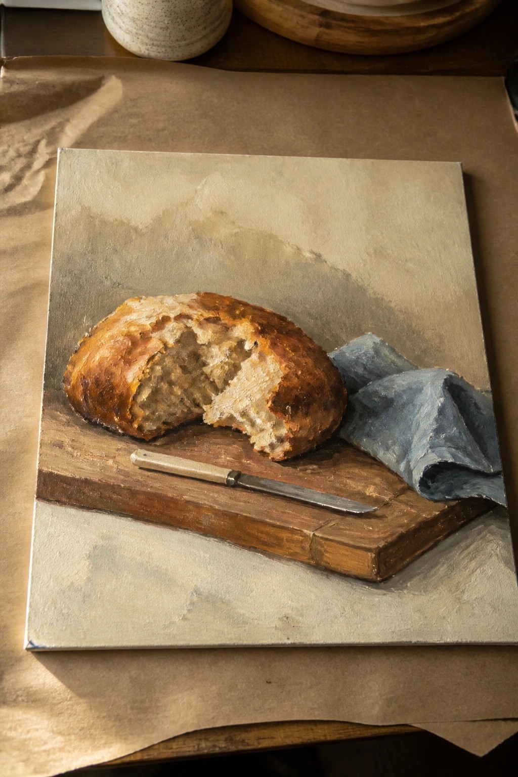 Crusty golden bread loaf missing a slice on wooden board with knife and blue cloth.