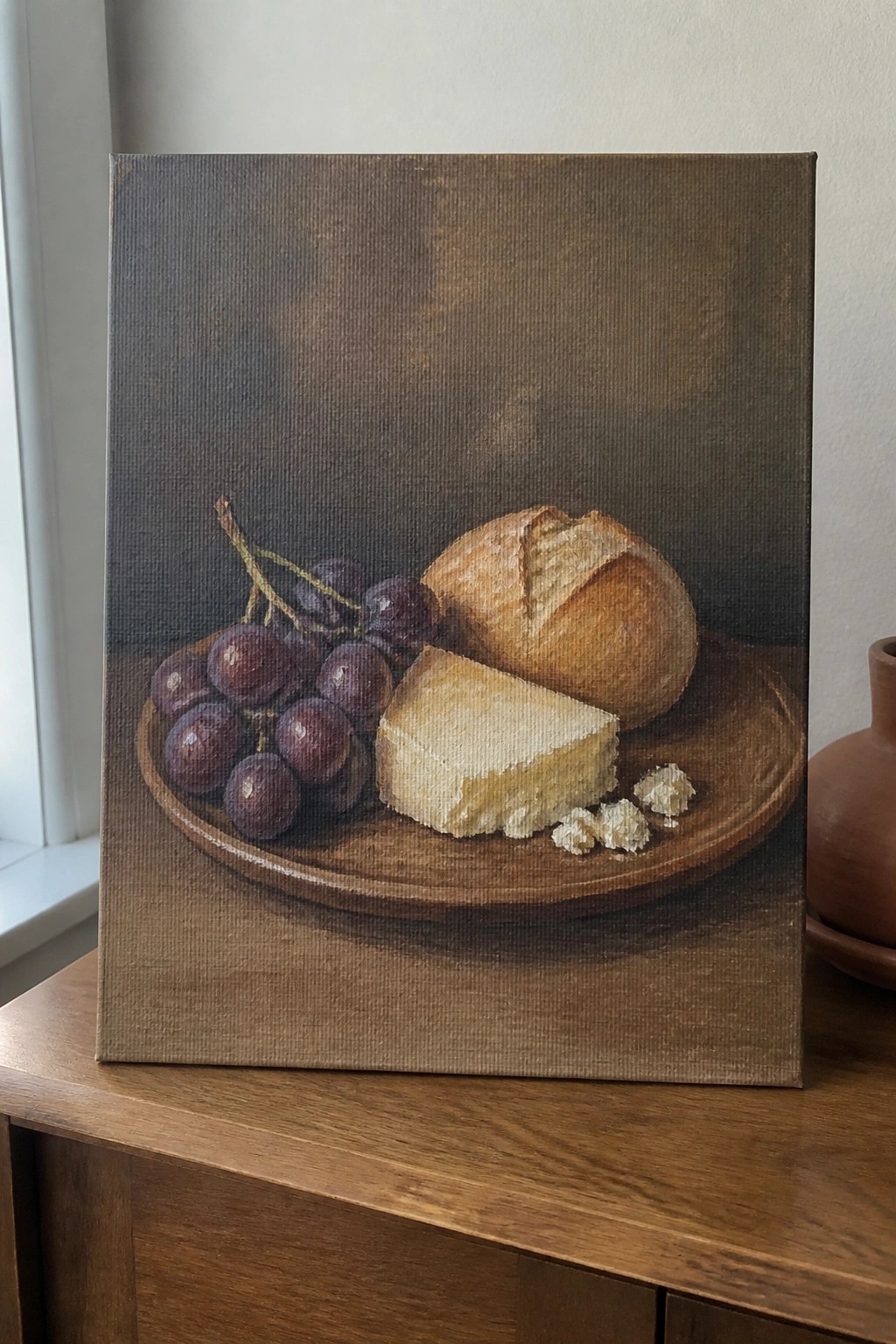 Still life painting of purple grapes, bread loaf, and cheese on wooden platter