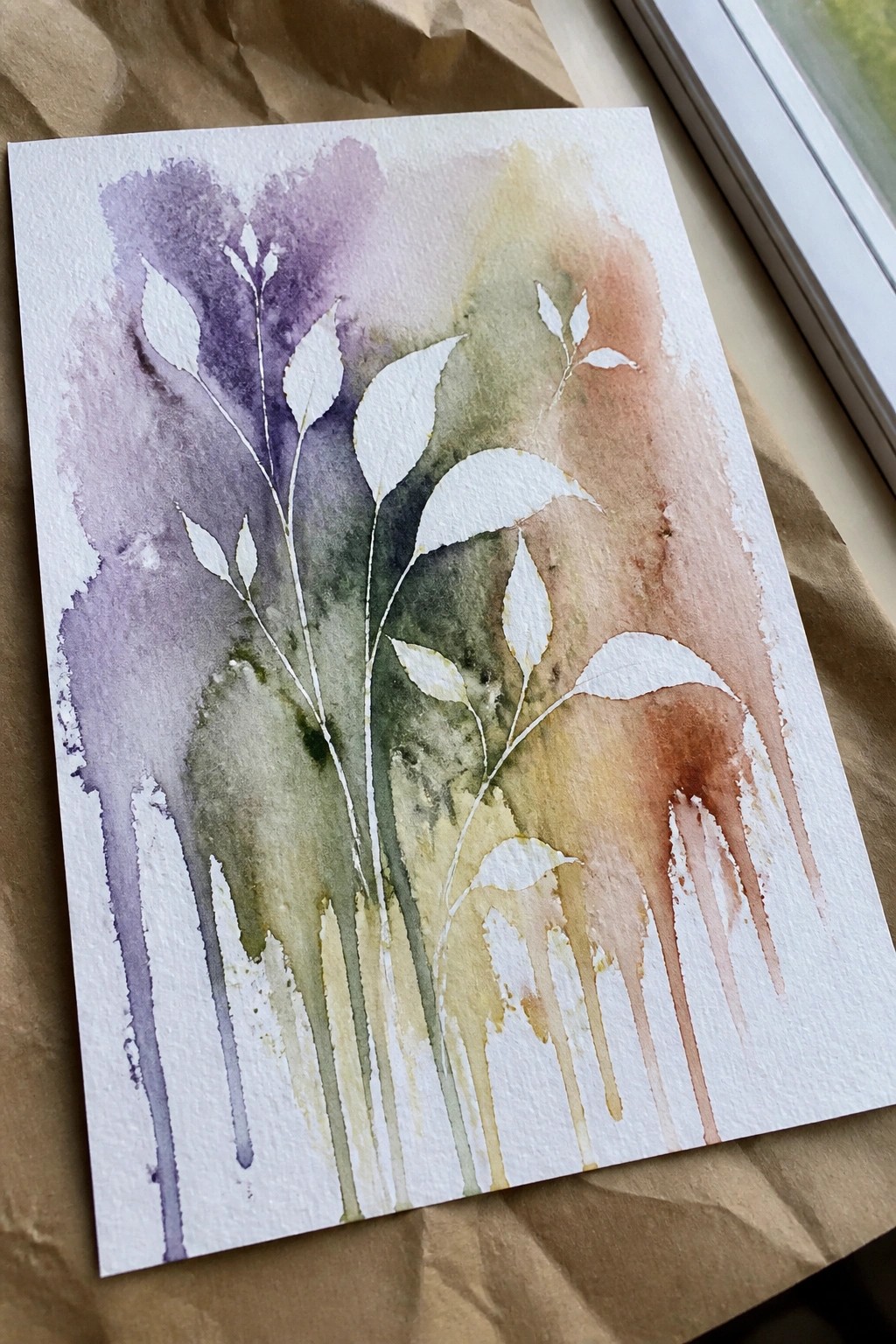 Watercolor painting of white leaves on purple green yellow and brown washes with drips