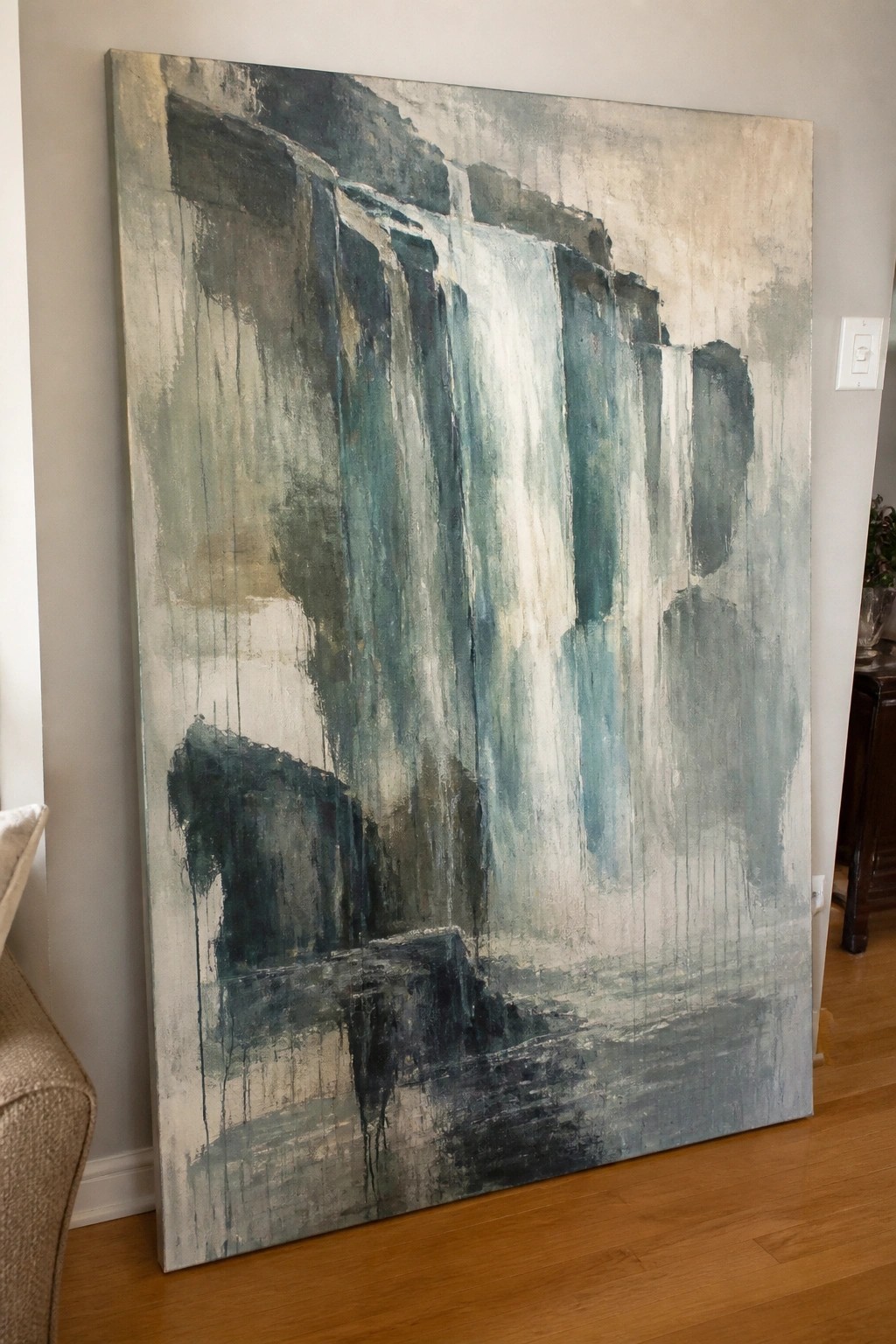 Large abstract painting with blue-green drips leaning on wooden floor against wall.