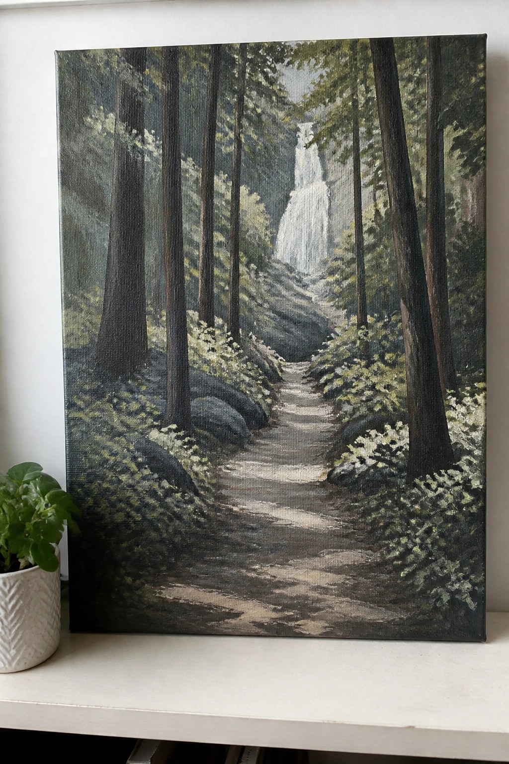 Oil painting of forest path to waterfall with tall trees beside potted green plant.