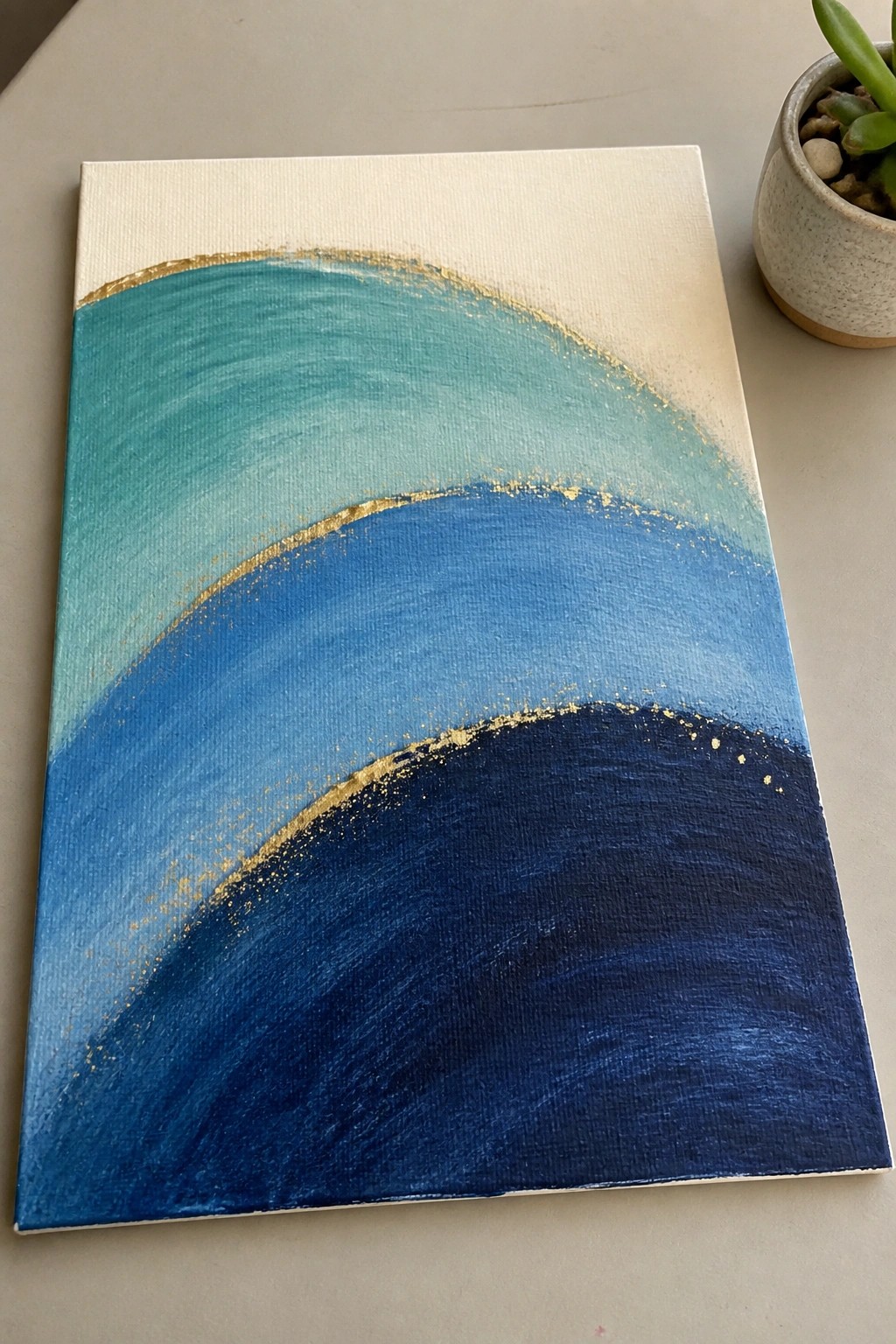 Abstract canvas painting with curved blue waves, gold accents, and potted plant.