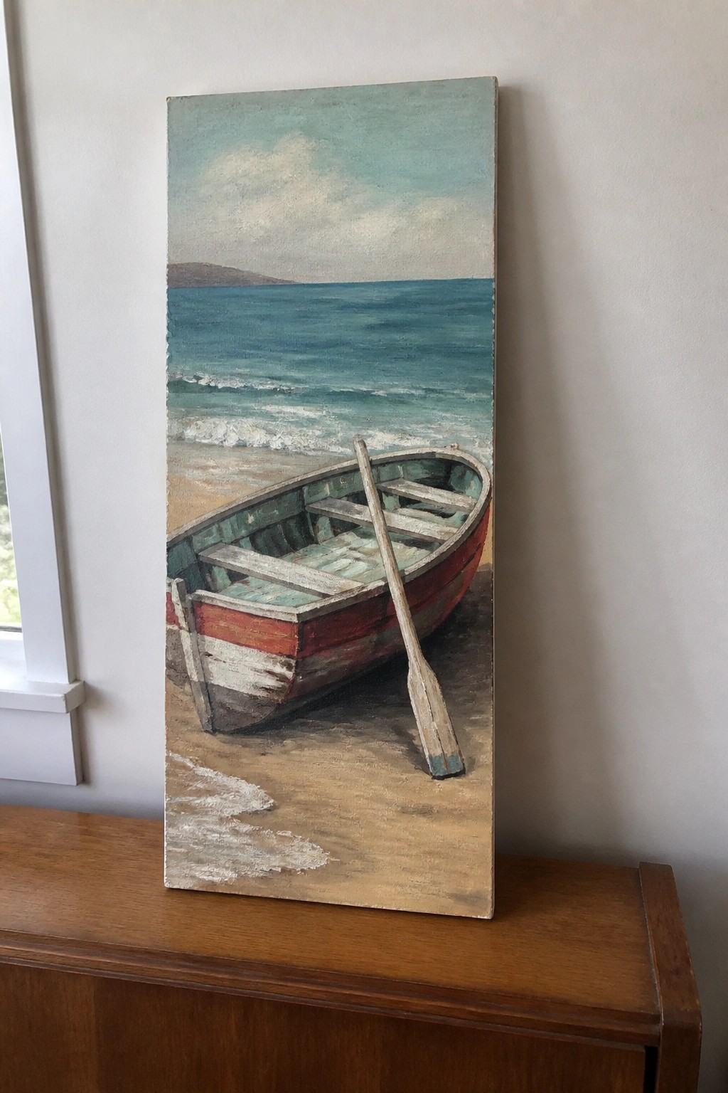 Red rowboat with oar on sandy beach beside turquoise ocean waves