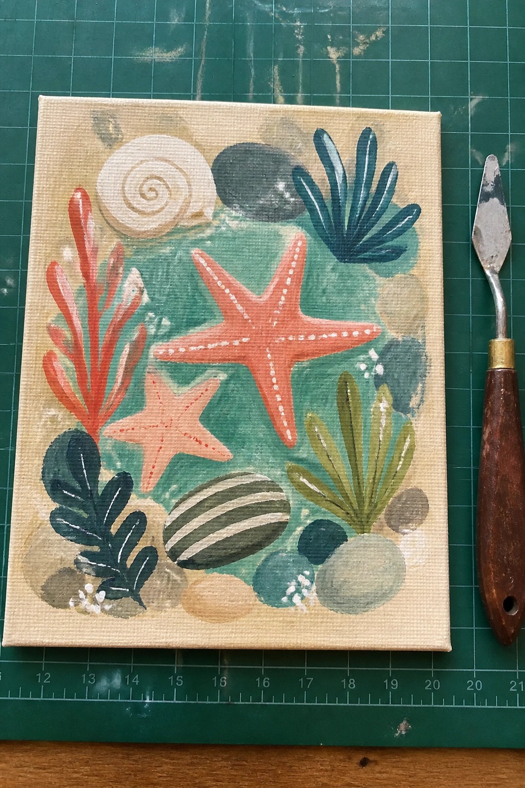 Vibrant sea life painting with orange starfish, red coral, shells on canvas beside knife.