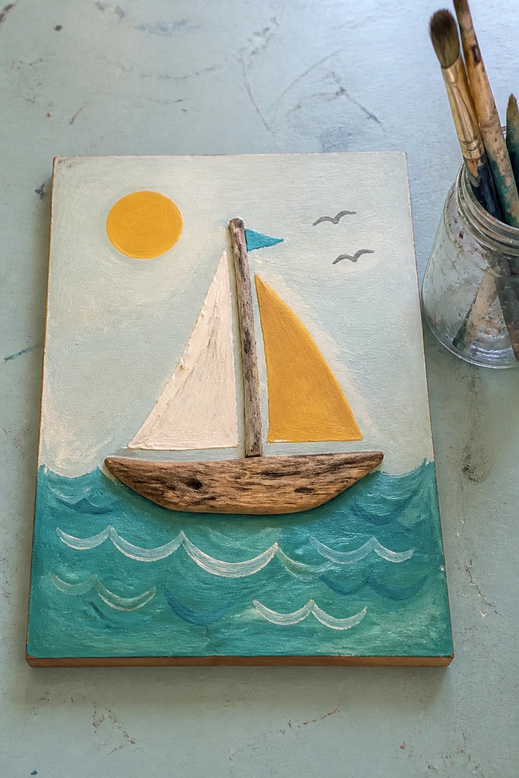 Driftwood sailboat collage with yellow sun, teal waves, white sails, and birds
