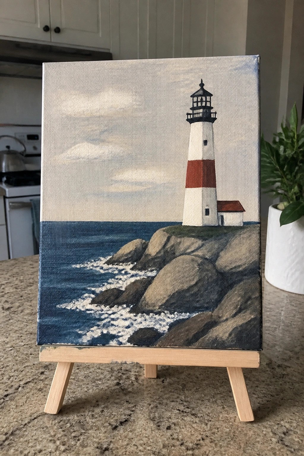Canvas painting of white-red lighthouse on rocky ocean cliffs atop wooden easel