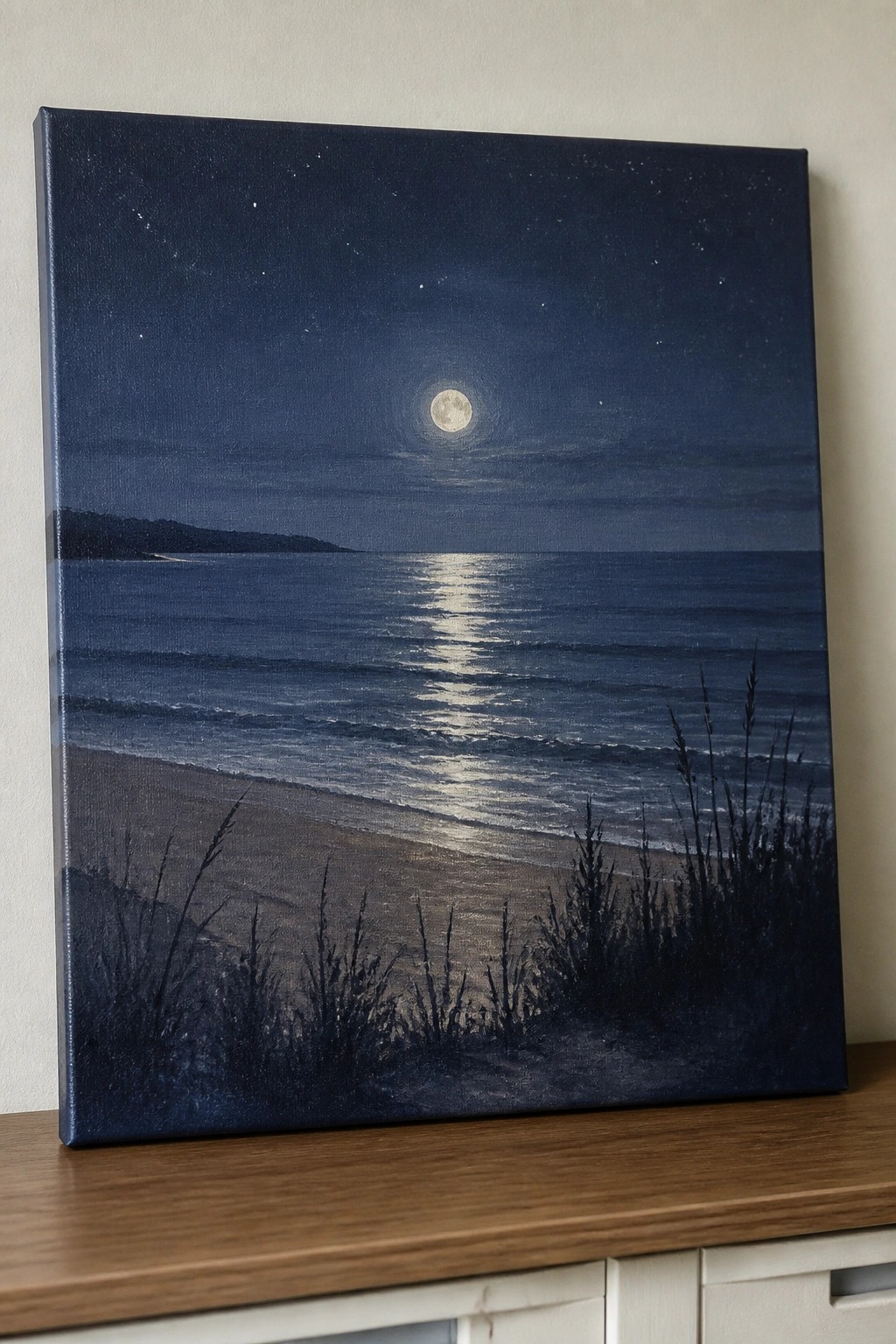 Moonlit ocean painting with moon reflection on waves, beach, and dark grass.