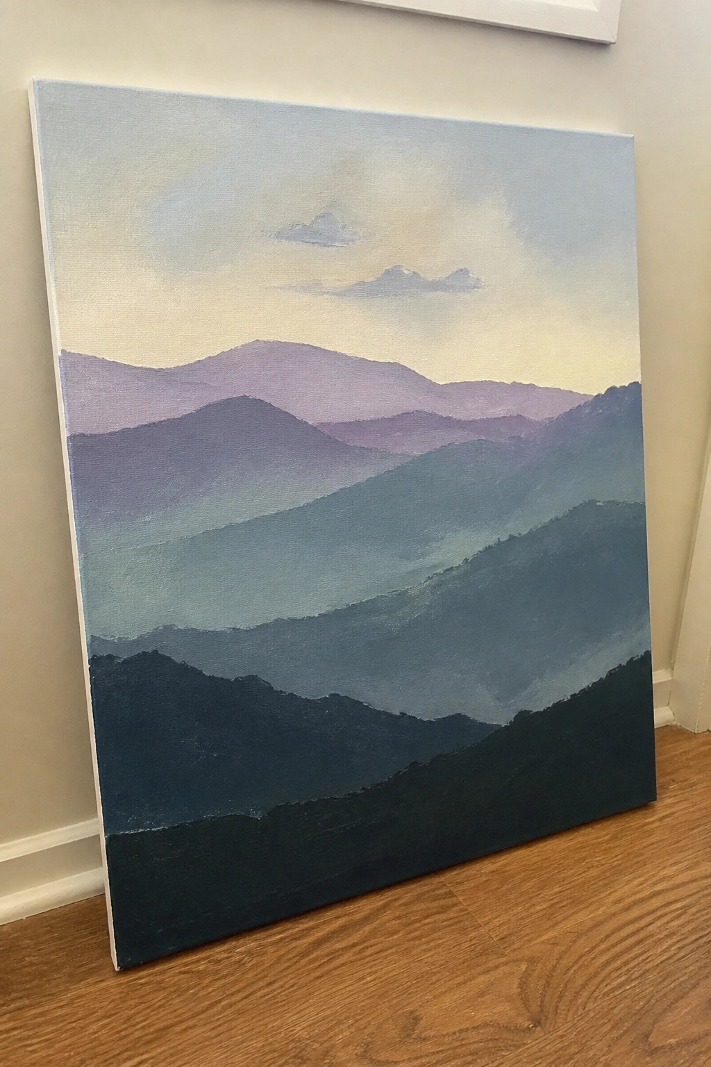 Layered blue and purple mountain landscape painting on canvas against a wall
