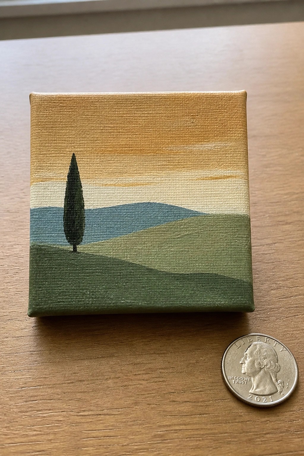 Tiny canvas landscape of lone tree on rolling green hills beside 2021 quarter