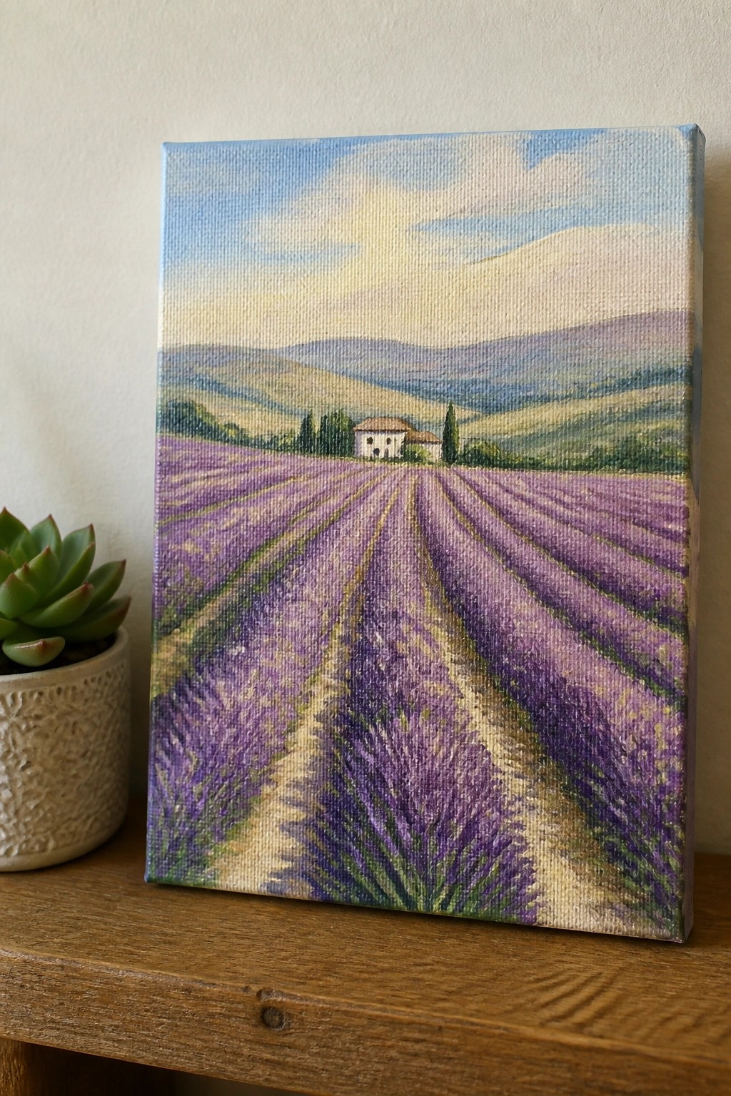 Painted canvas of purple lavender rows to house amid hills beside potted succulent