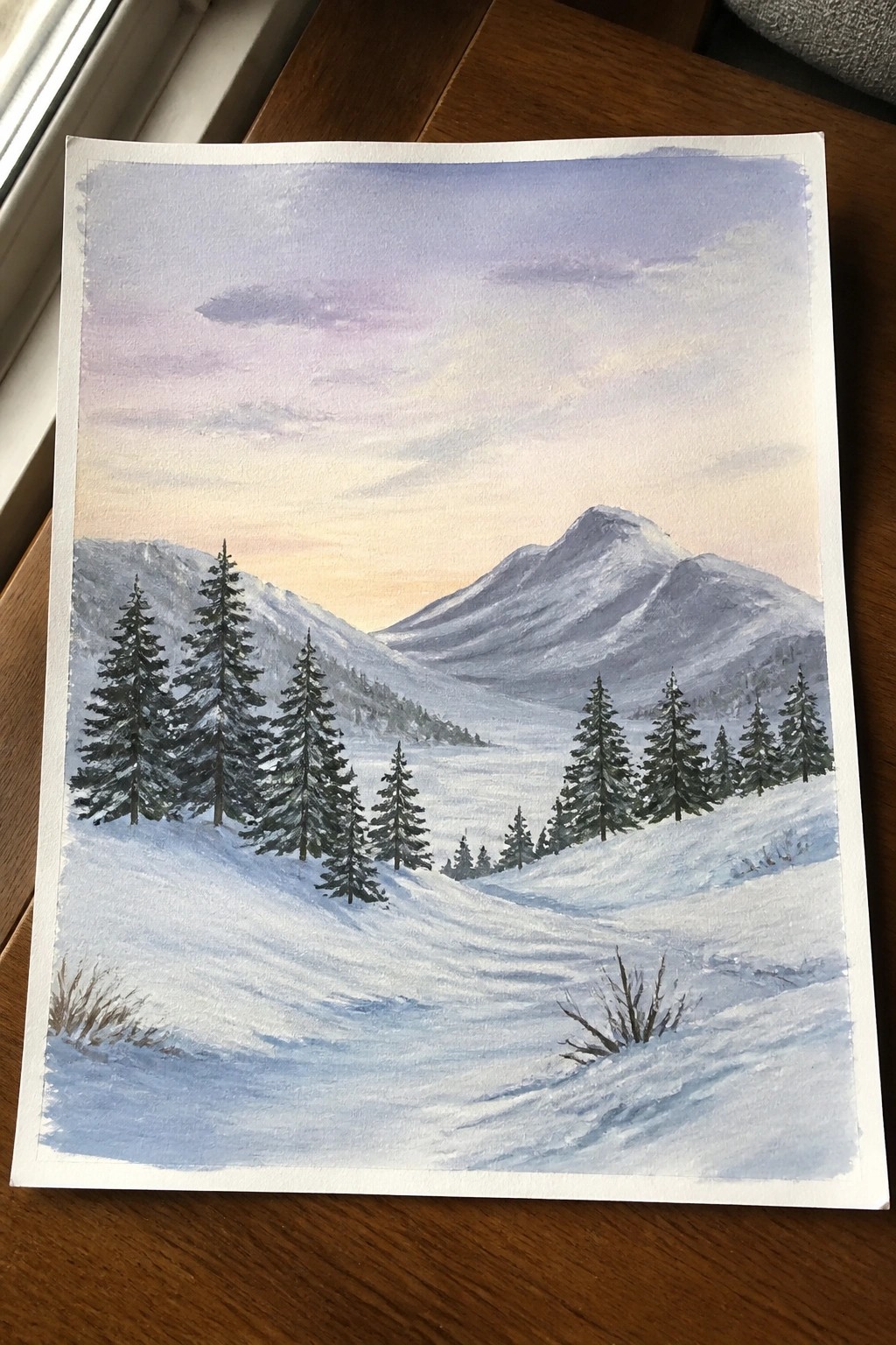 Watercolor of snowy mountain valley with pine trees, winding path, and pastel sunset sky.